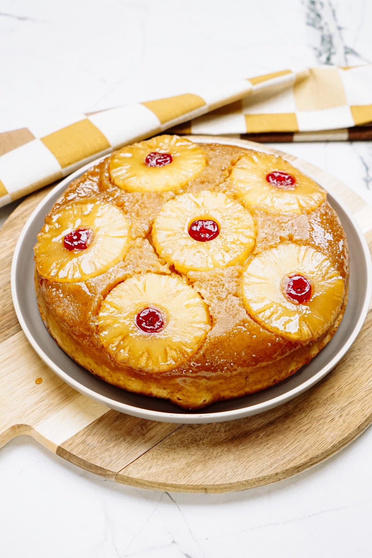Homemade pineapple upside-down cake on a plate, garnished with cherries and displayed on a wooden serving board.