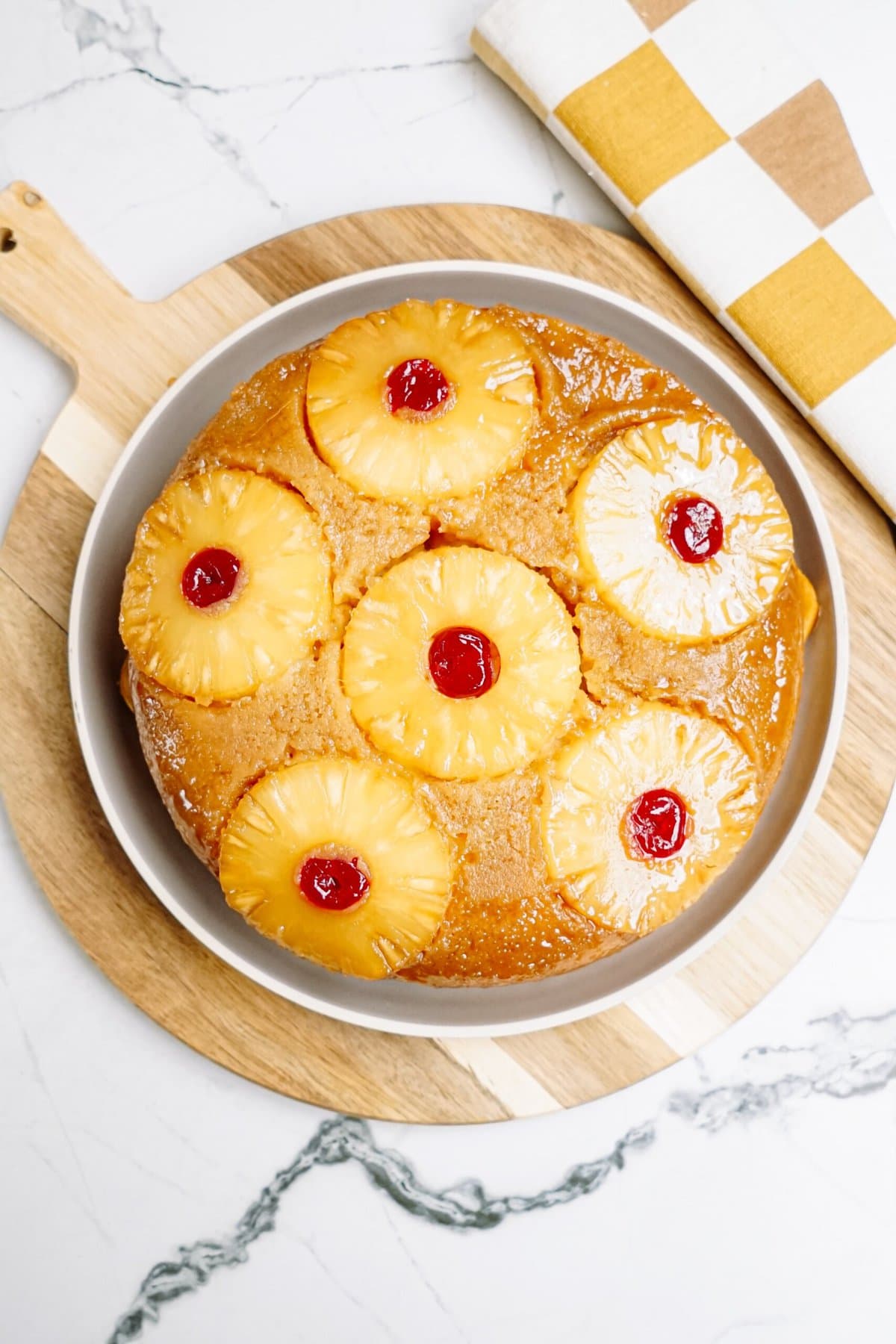 A pineapple upside-down cake with cherry garnishes, displayed on a table.