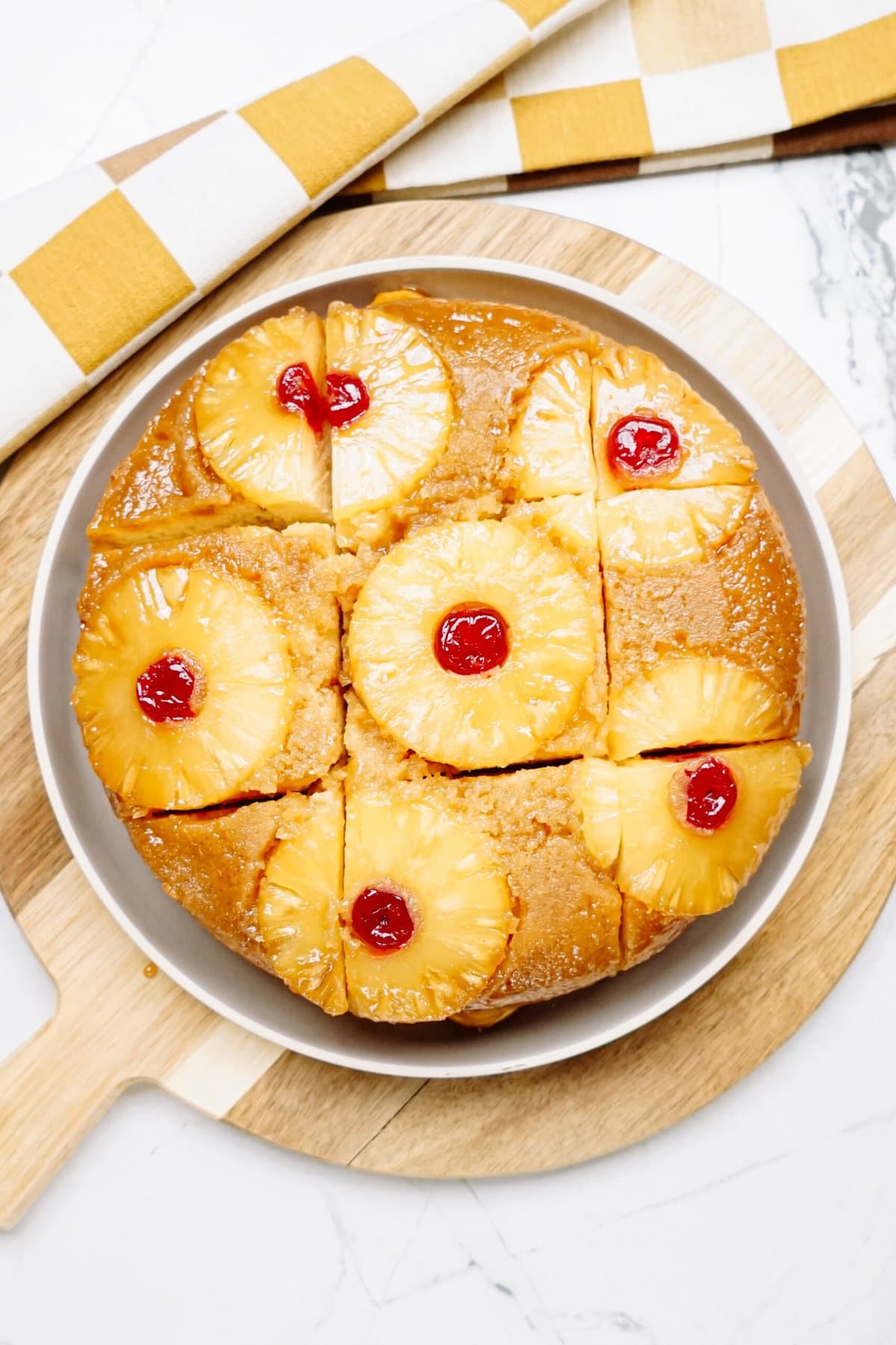 A pineapple upside-down cake on a wooden serving board, garnished with pineapple rings and maraschino cherries.