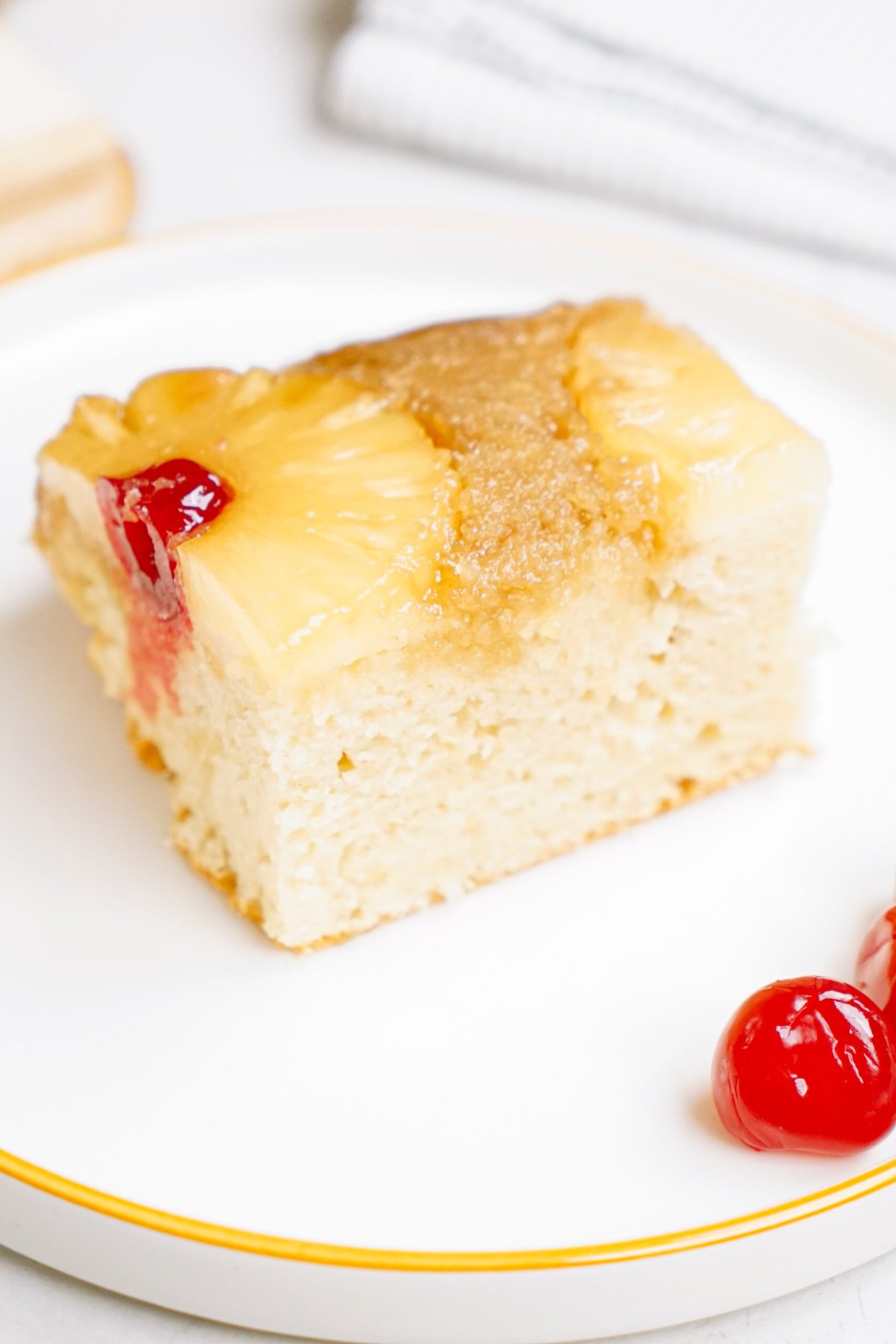 A slice of pineapple upside-down cake on a white plate with a cherry garnish.