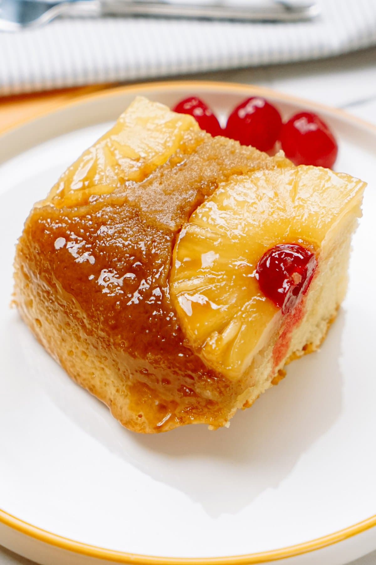 A slice of caramelized pineapple upside-down cake on a plate with cherries.