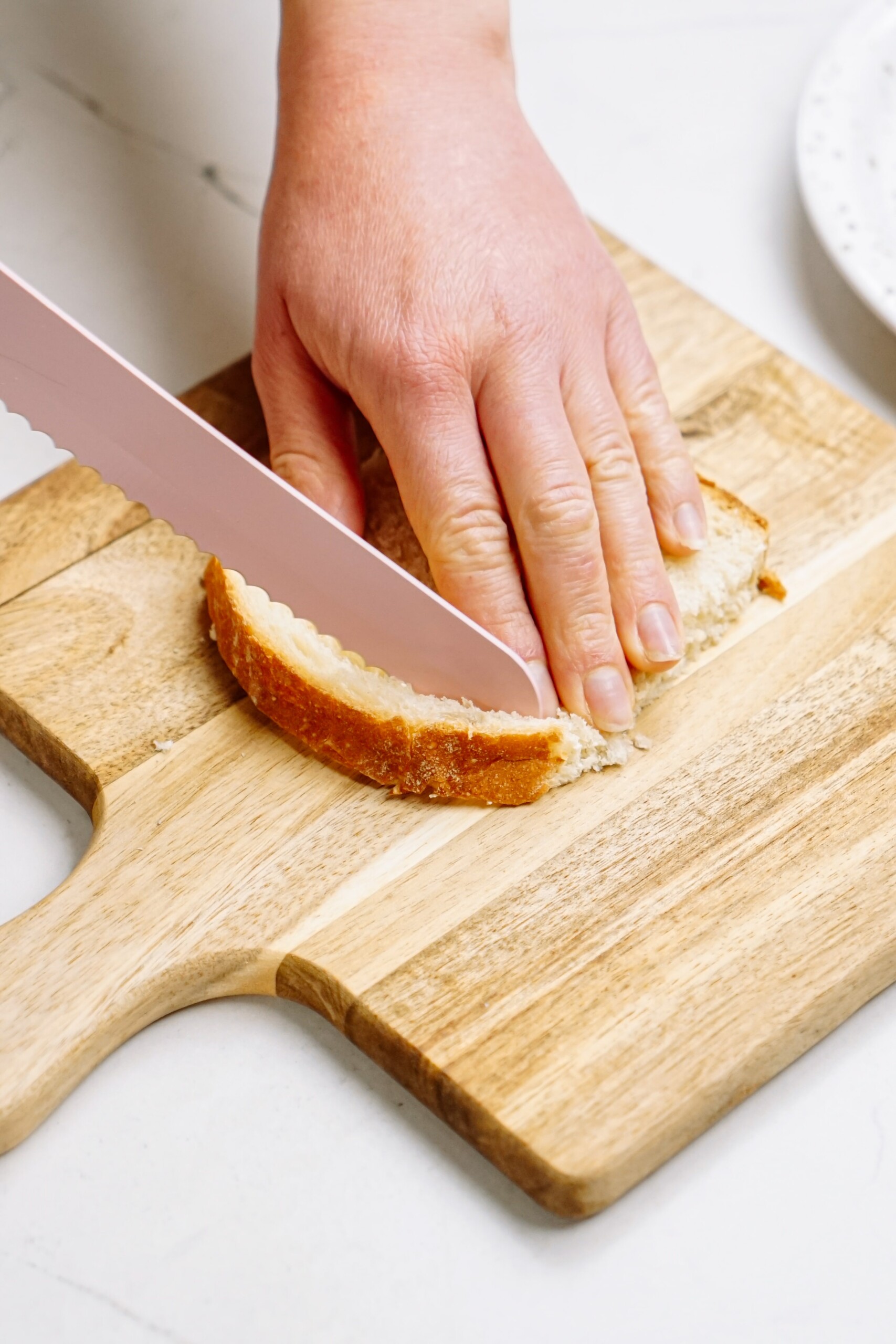 A person cutting a piece of bread on a cutting board for breakfast.