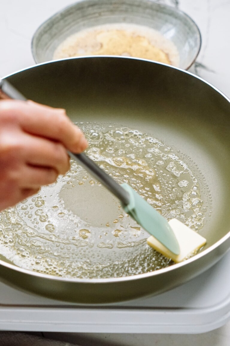 A person using a spatula to stir butter in a frying pan, preparing breakfast pigs in a blanket.