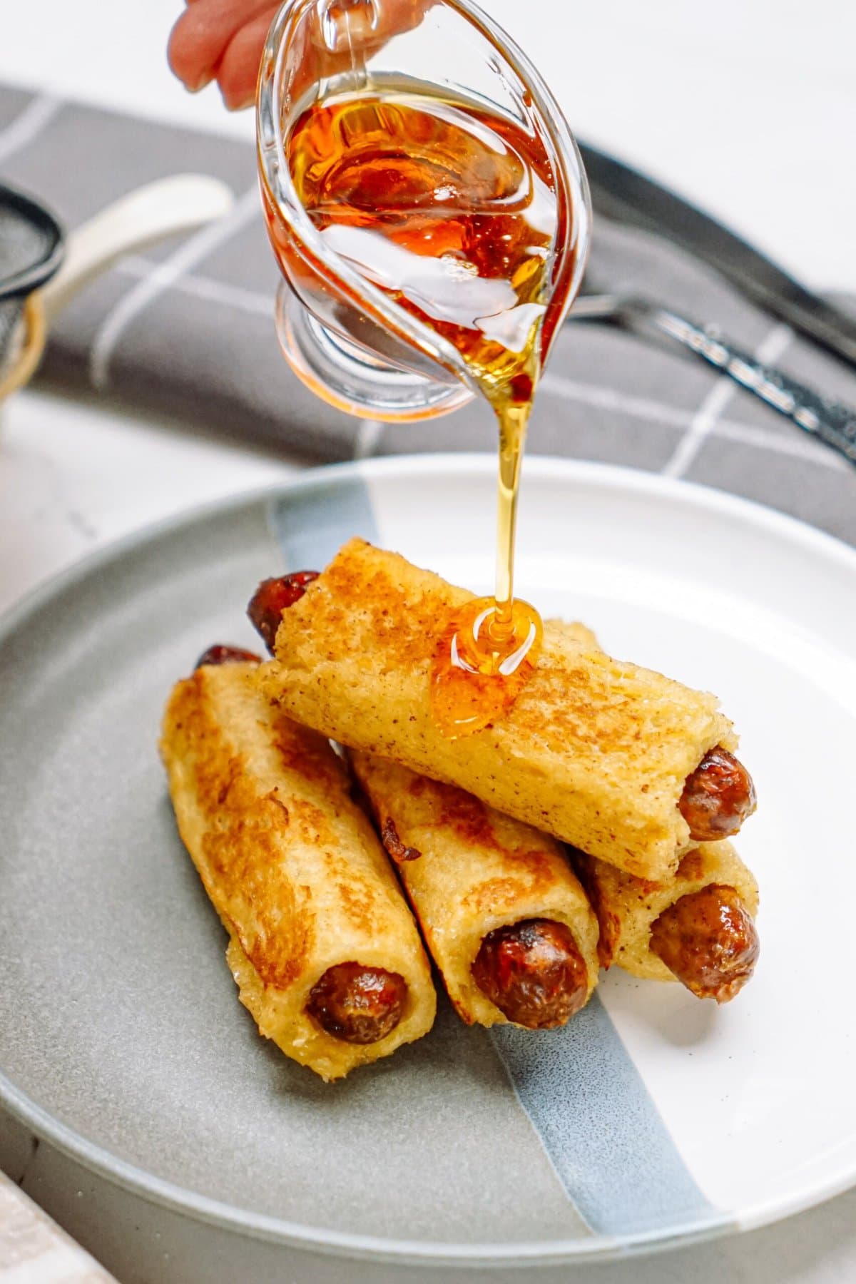 A person is drizzling syrup on a plate of breakfast pigs in a blanket.