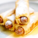 A breakfast plate of pigs in a blanket with powdered sugar.