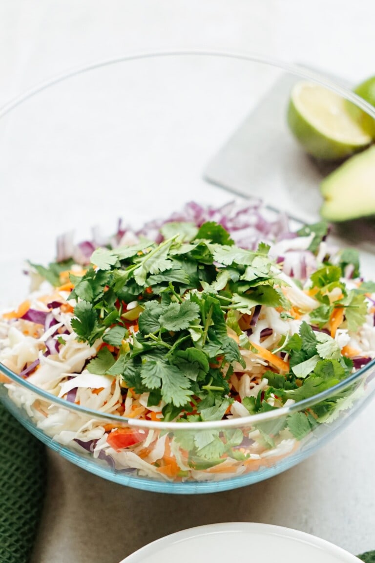 A fresh vegetable salad with cilantro garnish and fish tacos in a glass bowl.