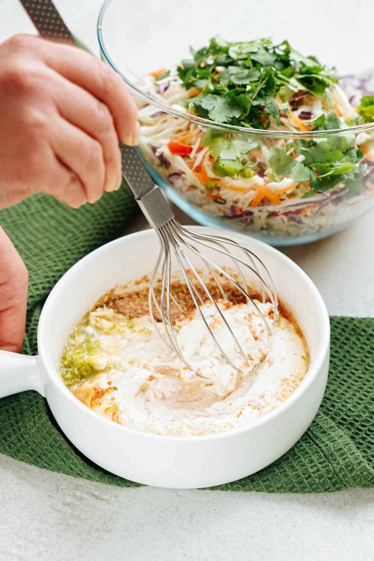 Whisking a dressing in a white cup with a green napkin underneath, with colorful fish tacos in the background.