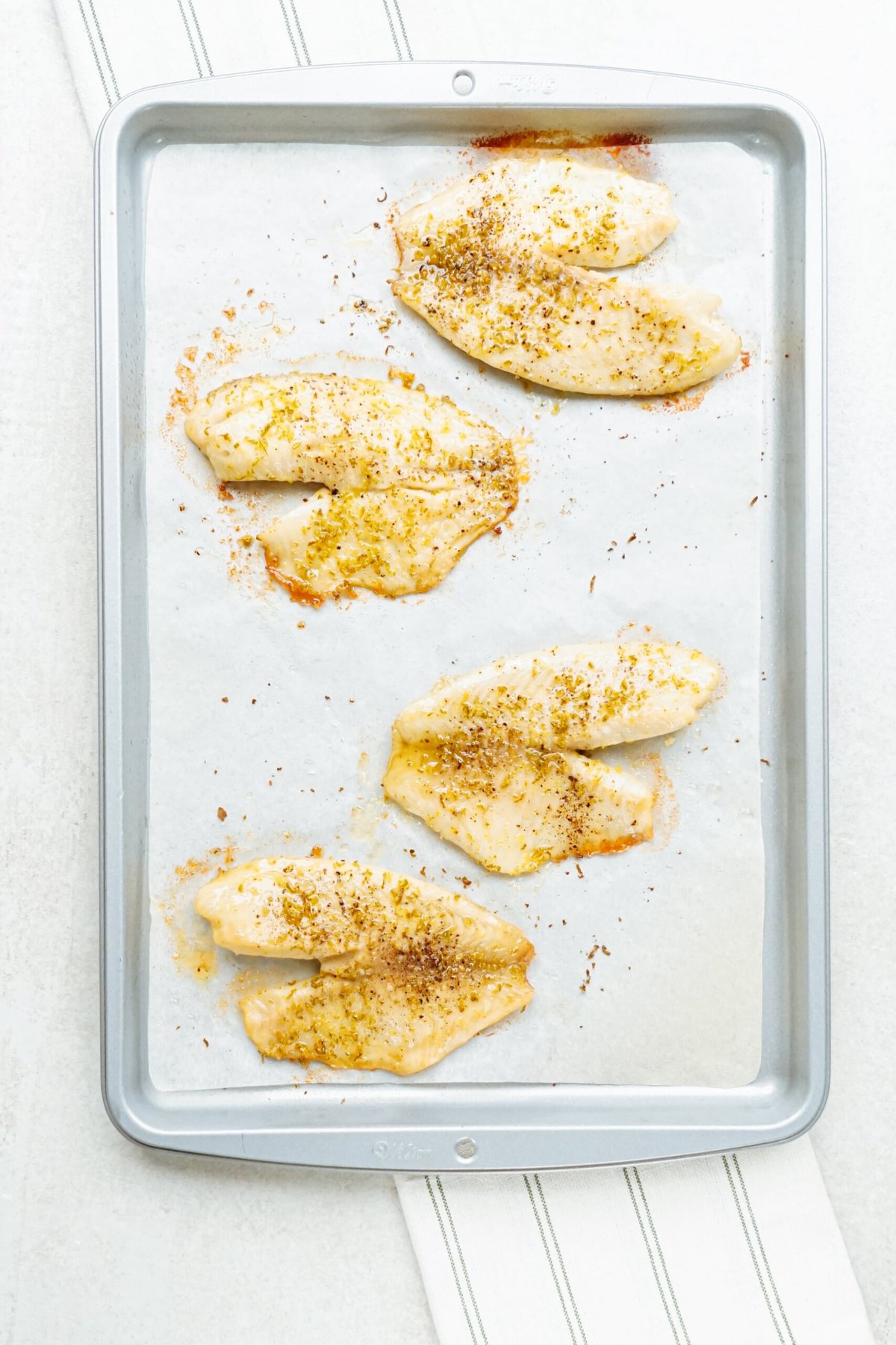 Marinated fish seasoned with spices on a baking tray lined with parchment paper for tacos.