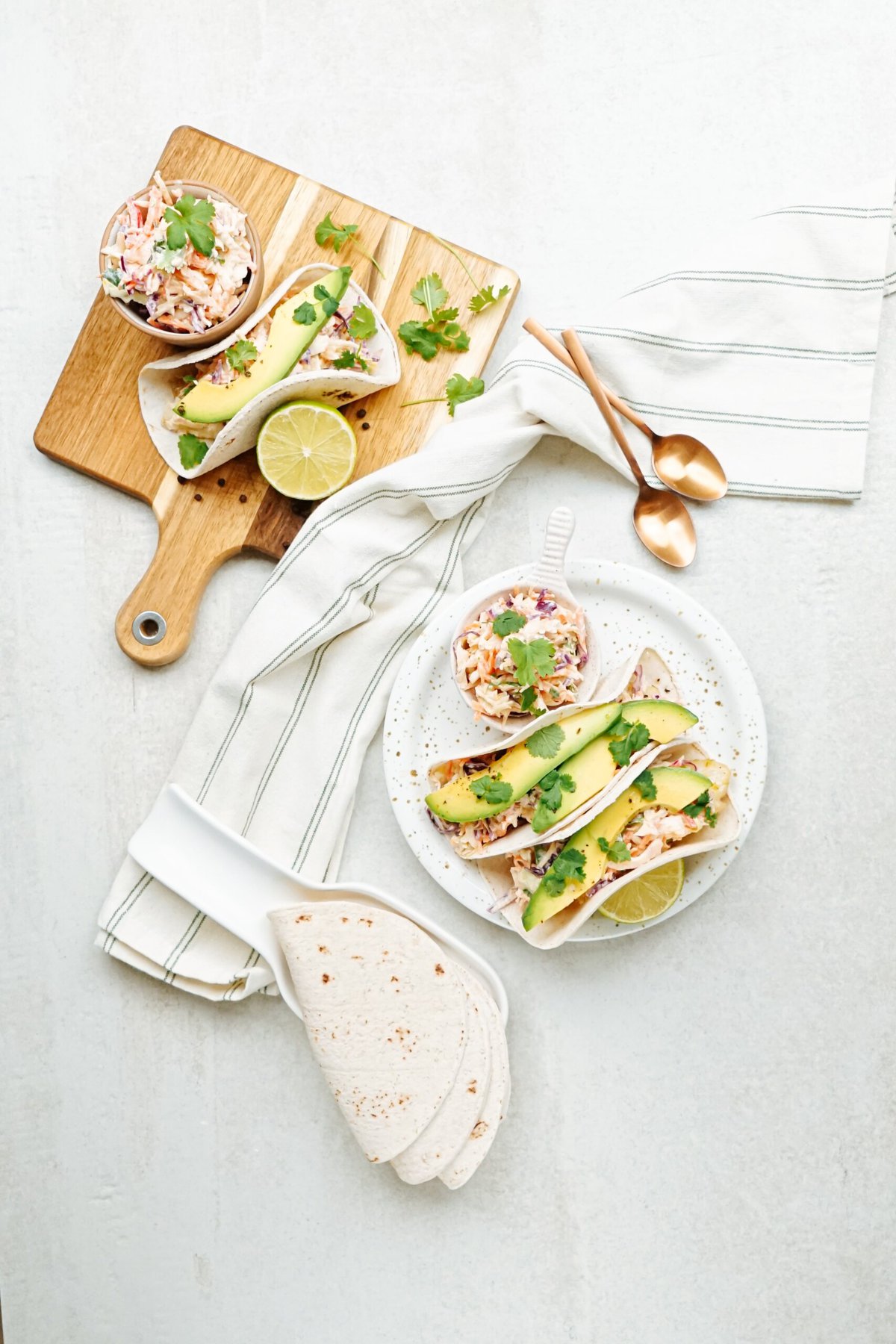 A spread of fish tacos and a bowl of coleslaw on a bright kitchen surface with culinary utensils.
