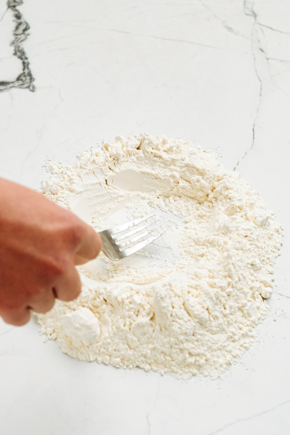A person using a fork to mix flour on the counter
