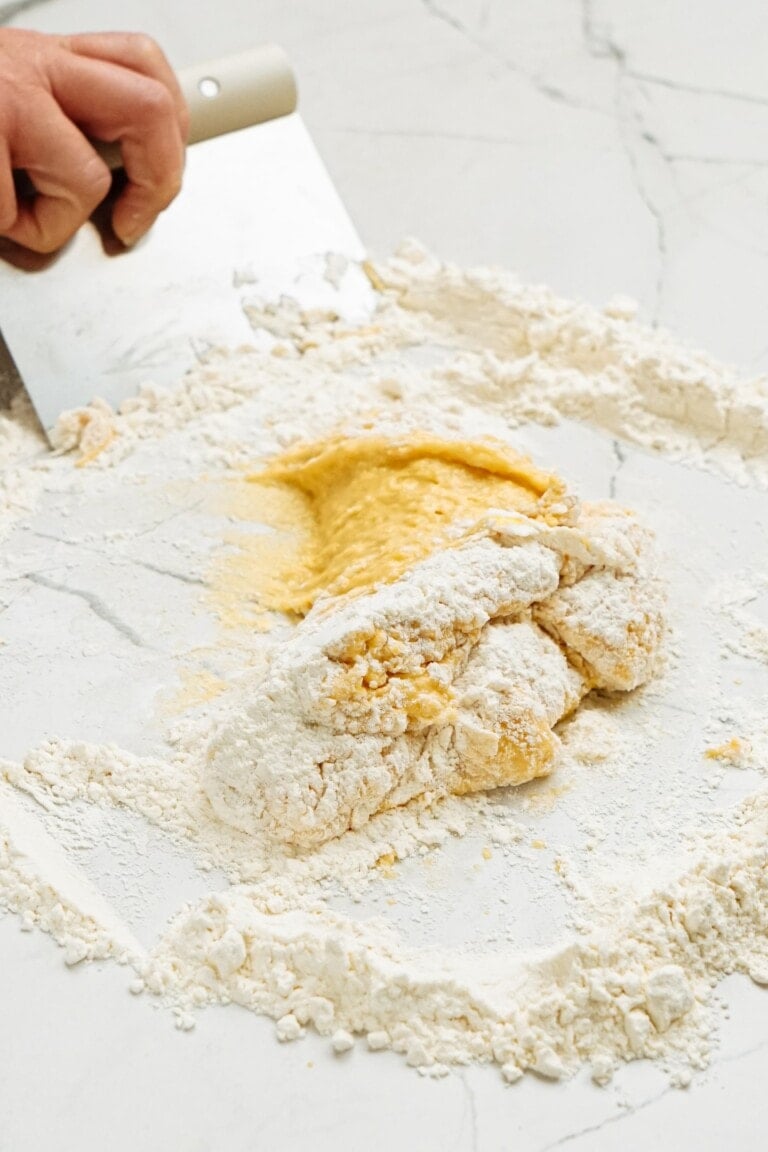 A person kneading dough on a white surface.