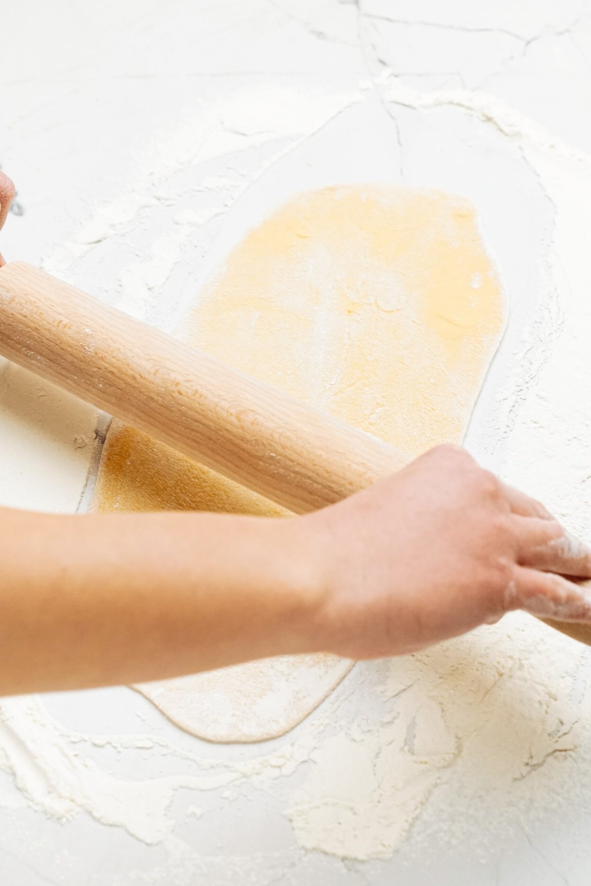 A person rolling out dough on a white surface.