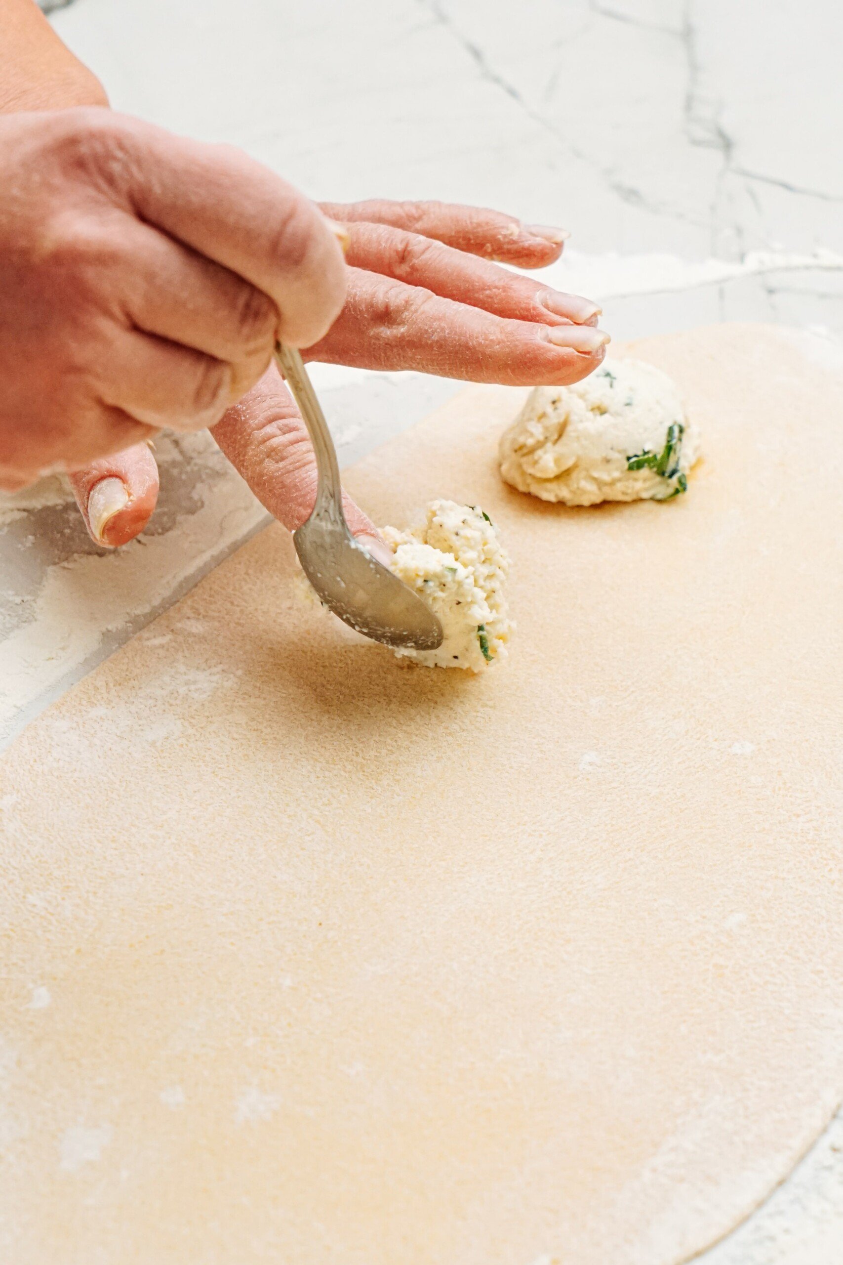 a person adding a spoonful of ravioli filling to the dough