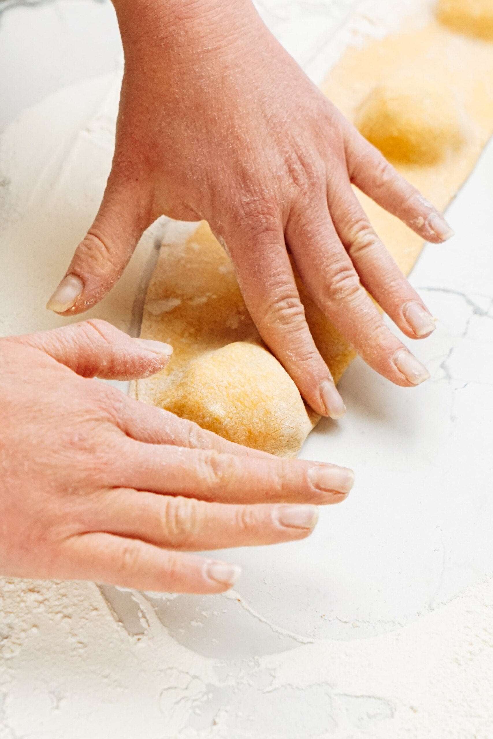 A woman's hands are pressing dough around ravioli filling