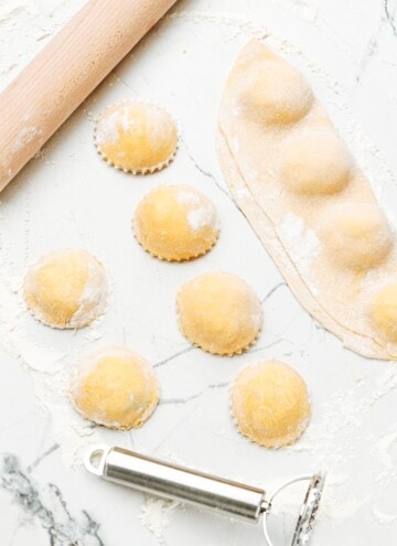 Ravioli on a marble countertop with a rolling pin.