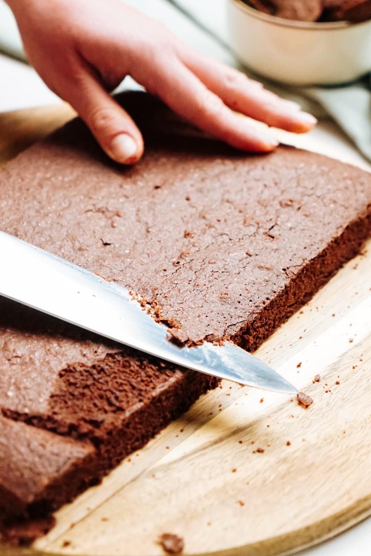 A person cutting the top of chocolate cake on a cutting board.