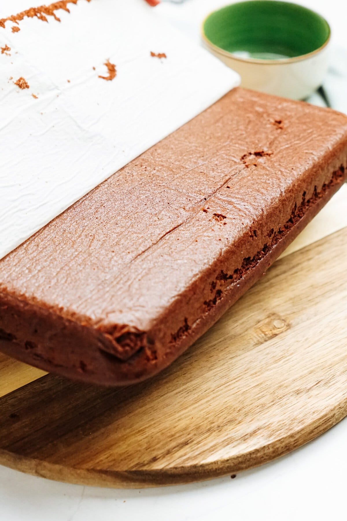A piece of chocolate cake on a wooden cutting board.