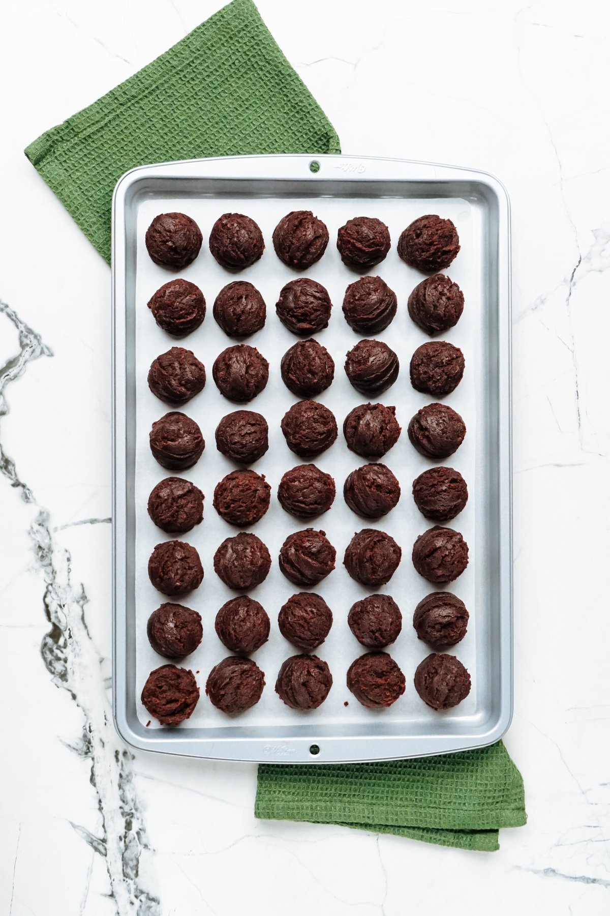 Chocolate truffles on a baking sheet with a green cloth.