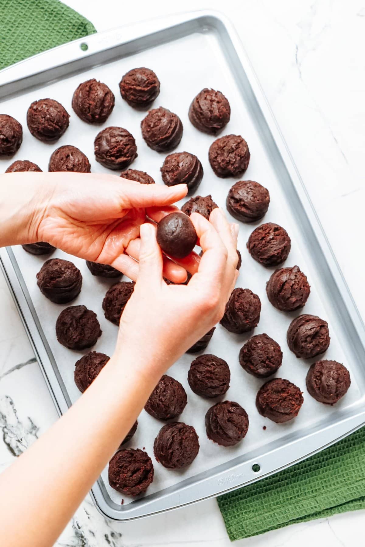 A person putting chocolate balls on a baking sheet.