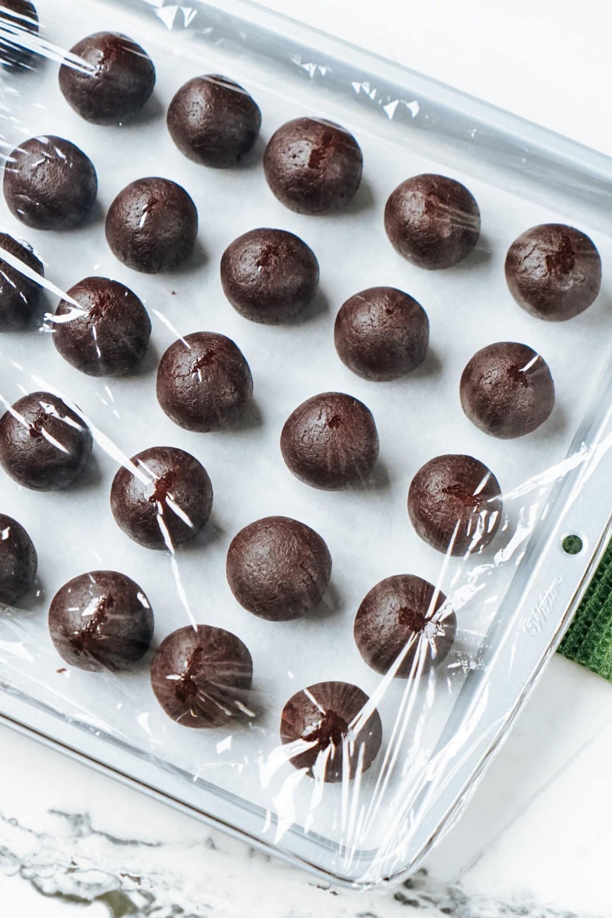 Chocolate truffles on a baking sheet covered in plastic wrap.