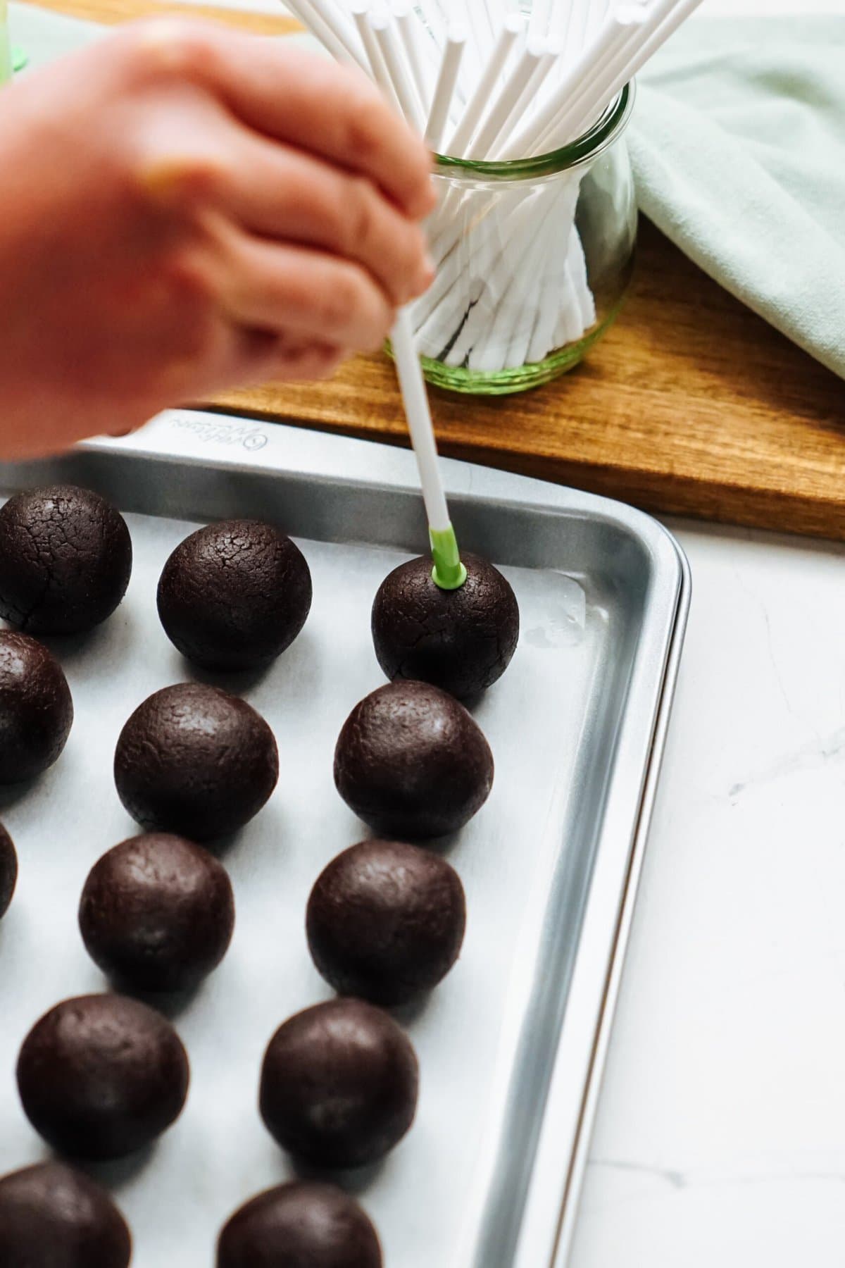 A person is putting a cake pop stick in chocolate balls on a baking sheet.