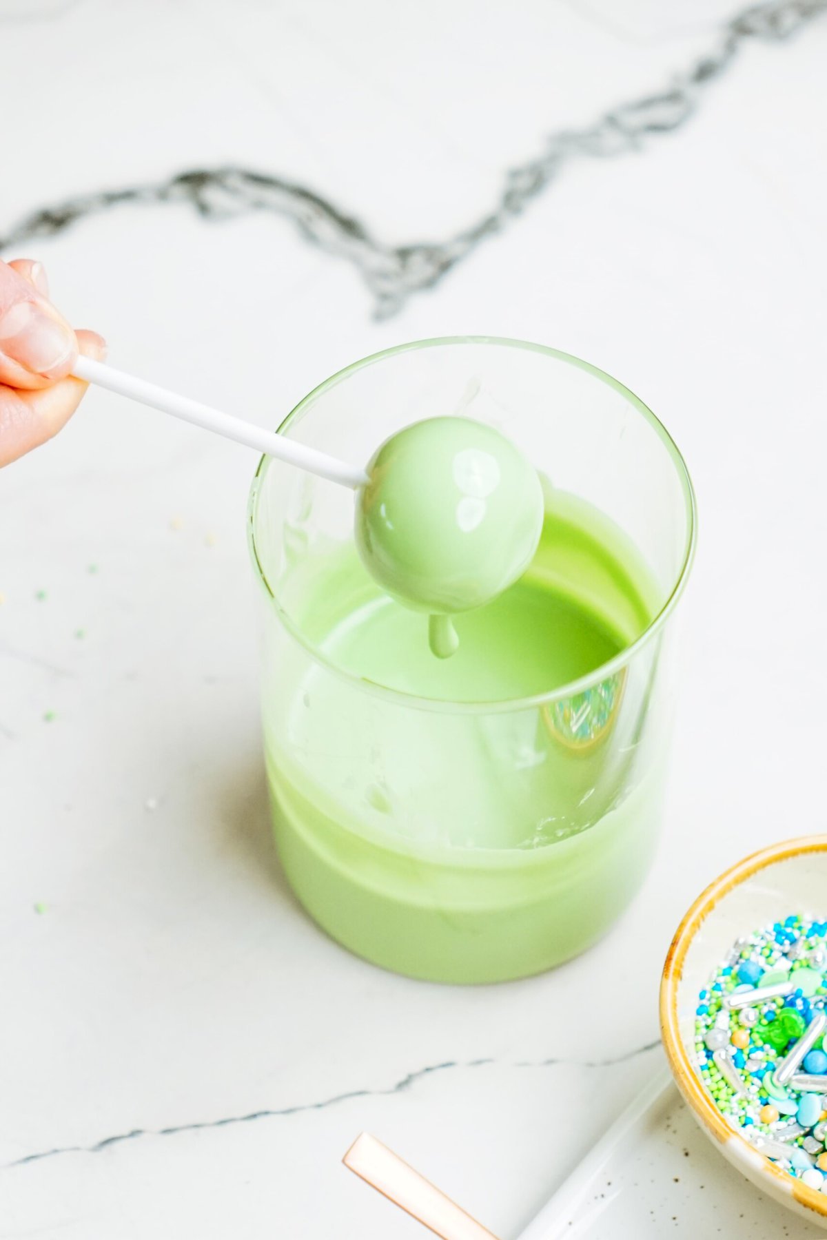 A person dipping a cake pop in melted green candy coating
