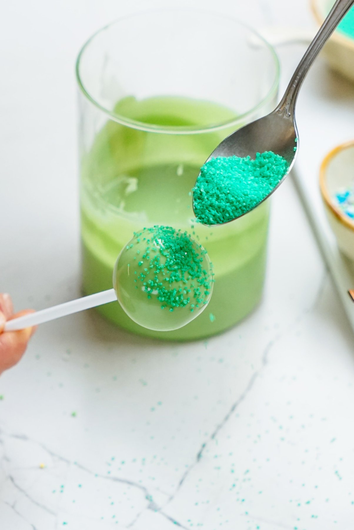 A person pouring green sprinkles onto a cake pop