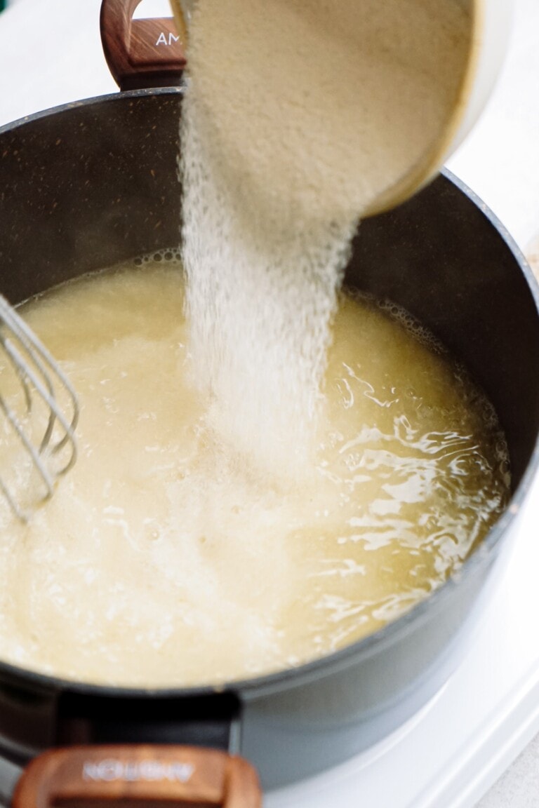 pouring grits into a pan of water with a whisk.