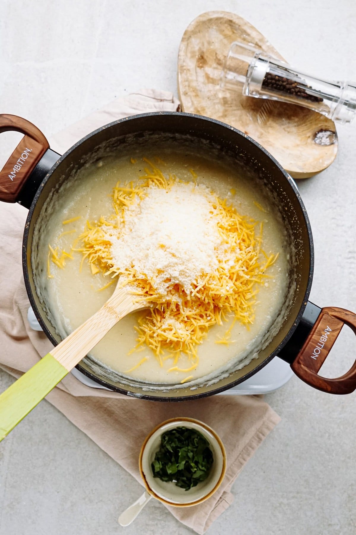 A pot of grits and shredded cheese with a wooden spoon.