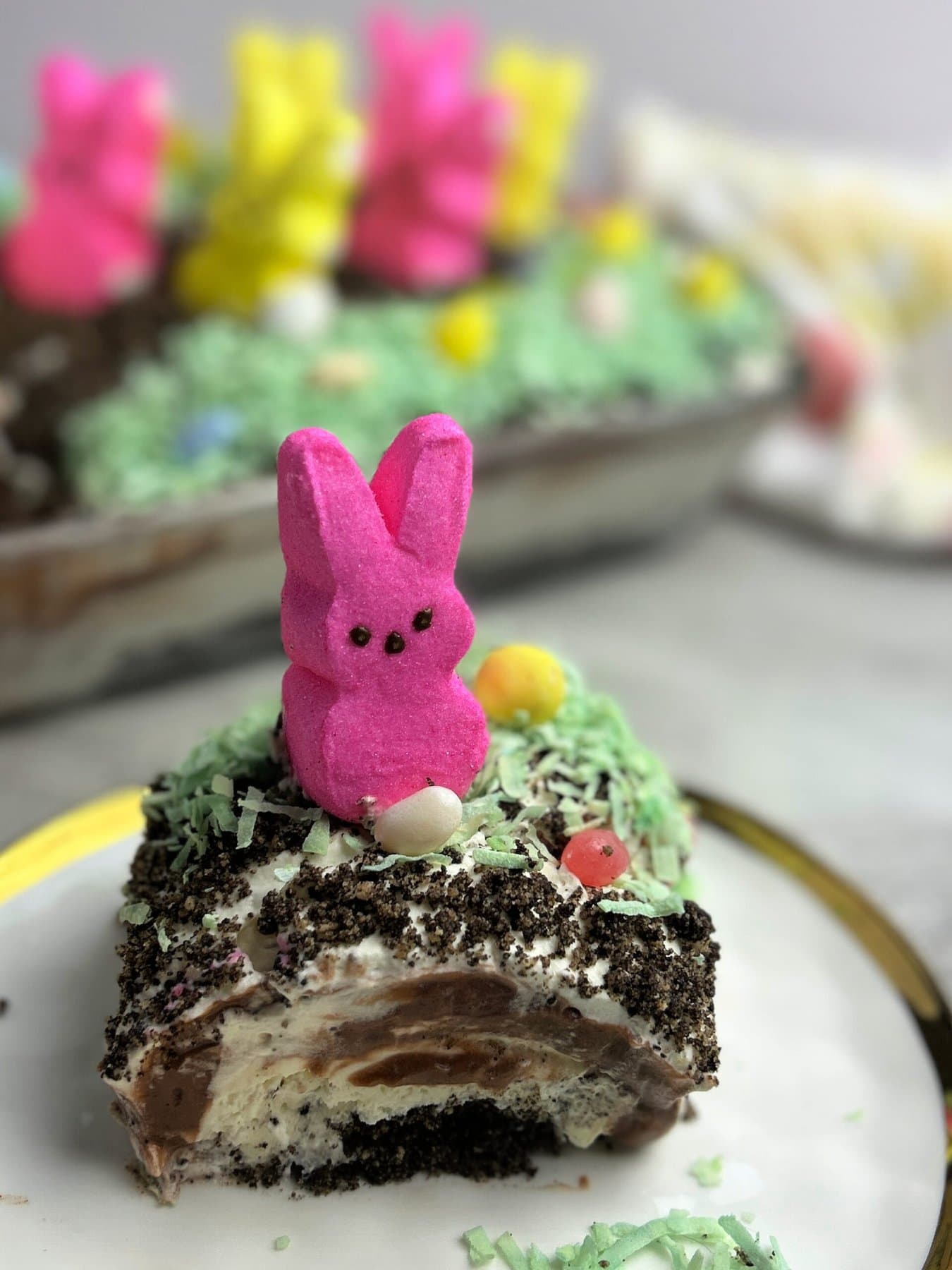 A slice of cake decorated with a pink marshmallow bunny and pastel sprinkles on a white background.