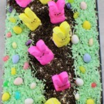A dessert resembling a garden with colorful marshmallow bunny candies and egg-shaped candies arranged on top of a layer of green coconut shavings and crumbled chocolate cookies.