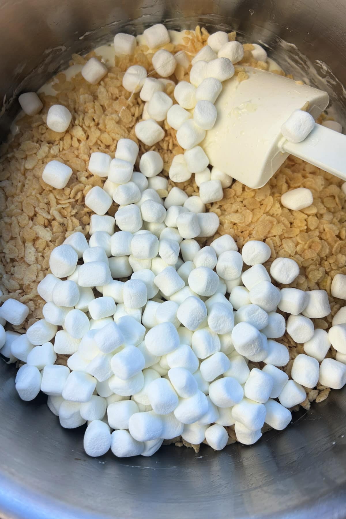 Ingredients for making Rice Krispie Treats, including cereal and marshmallows, in a mixing bowl with a spatula.
