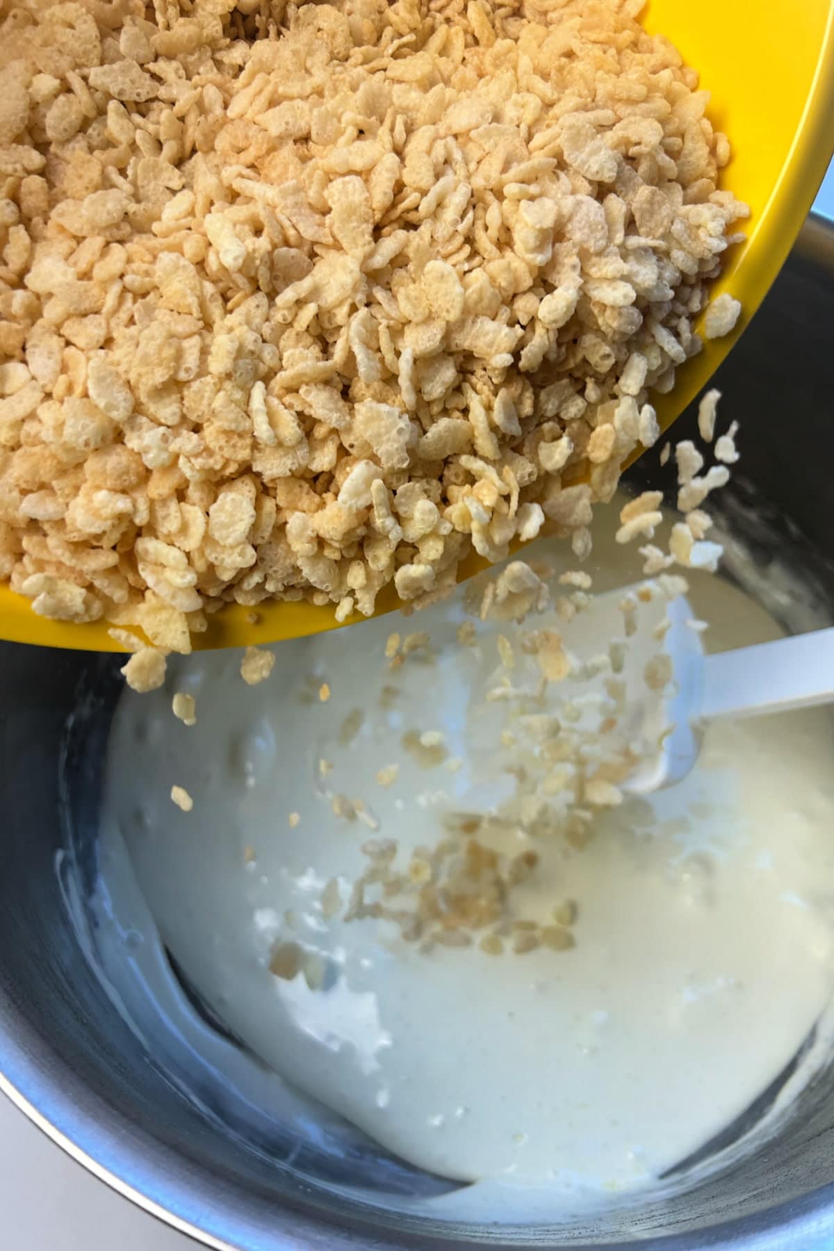 Pouring Rice Krispie Treats cereal from a yellow bowl into a bowl with milk.