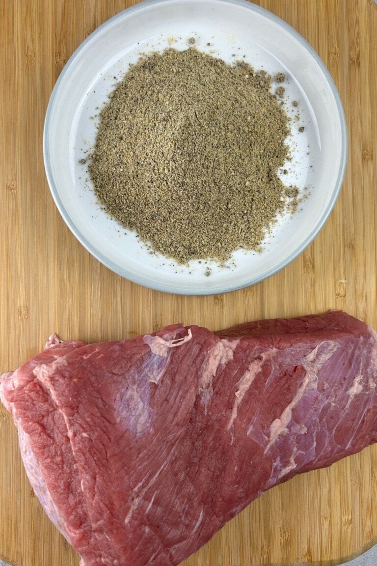 A piece of corned beef and a bowl of spices on a cutting board.