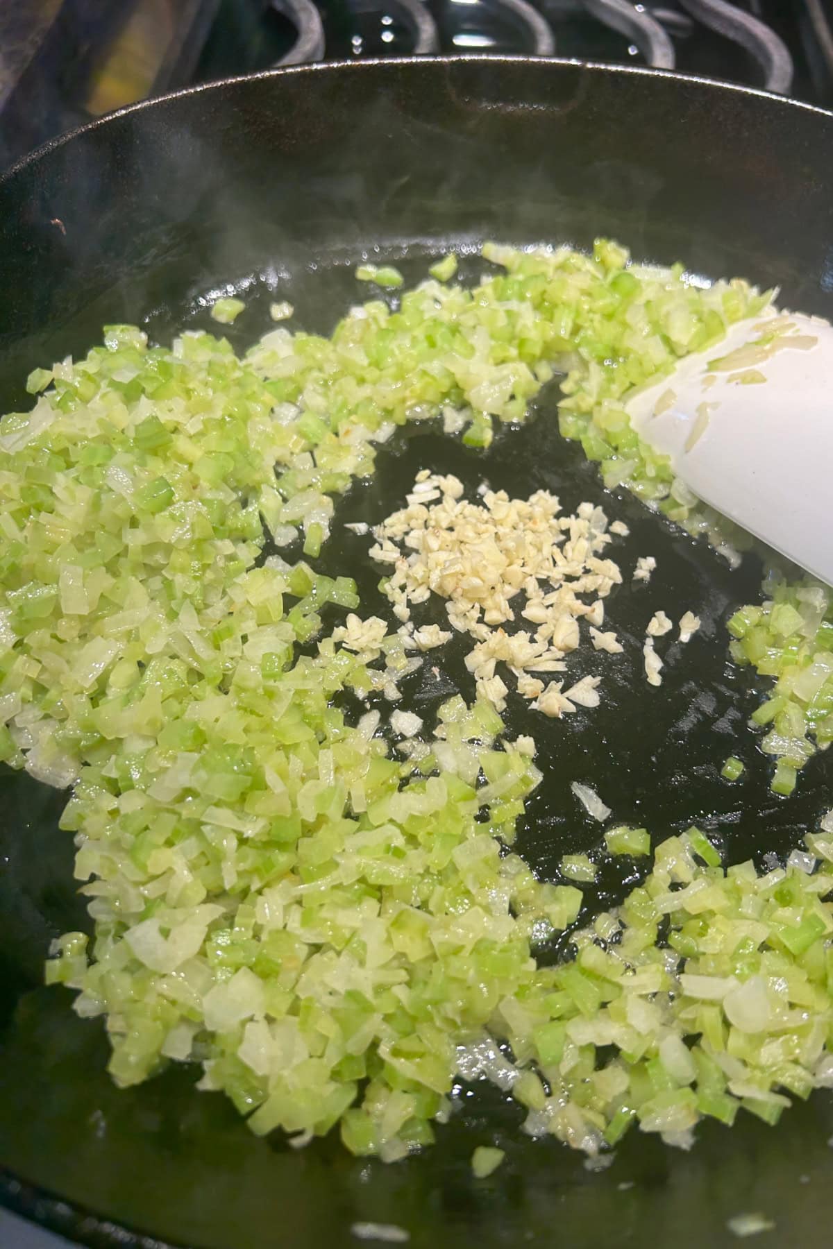 celery and onions sautéing with the addition of minced garlic to the pan 