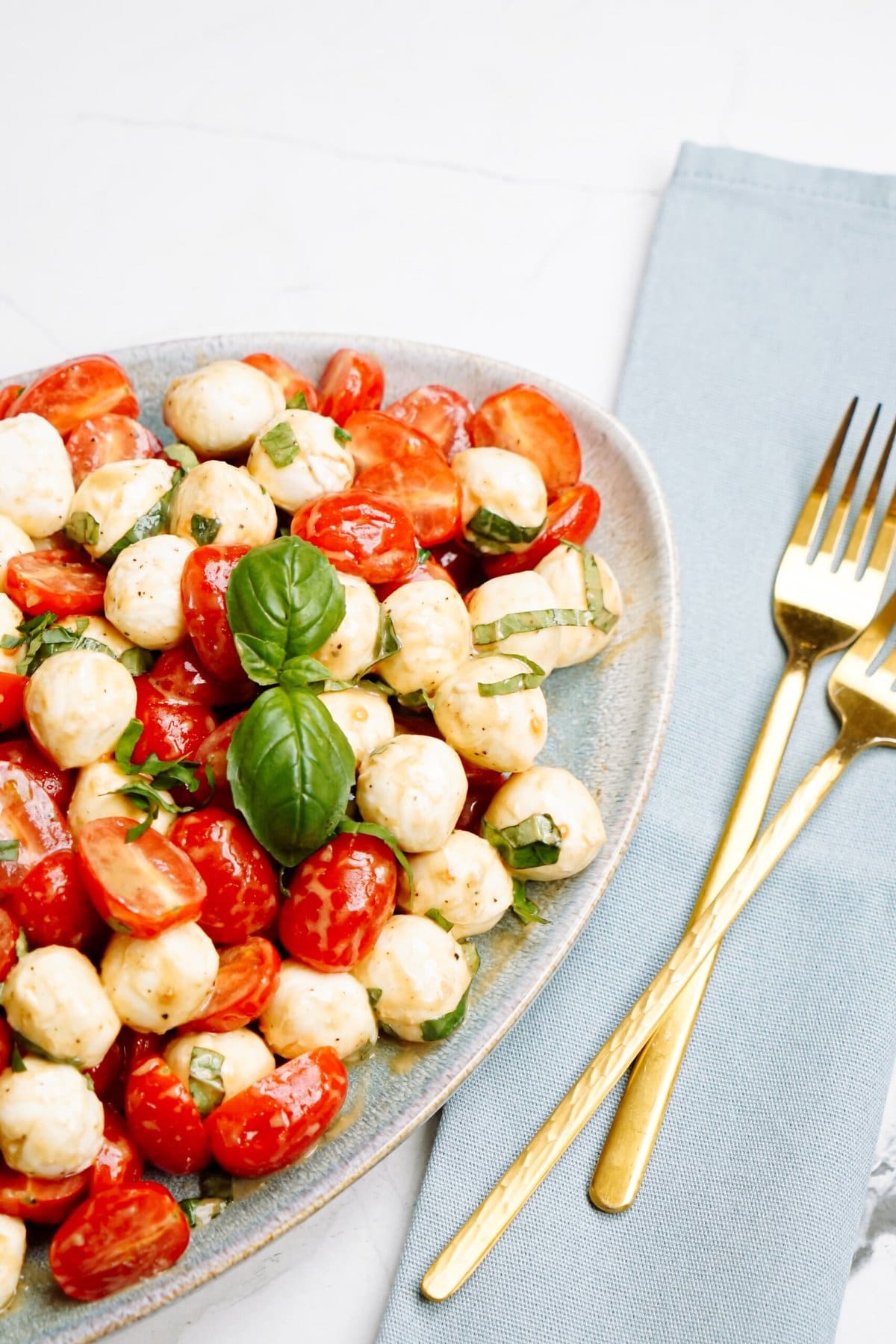 caprese salad on a plate next to 2 gold forks