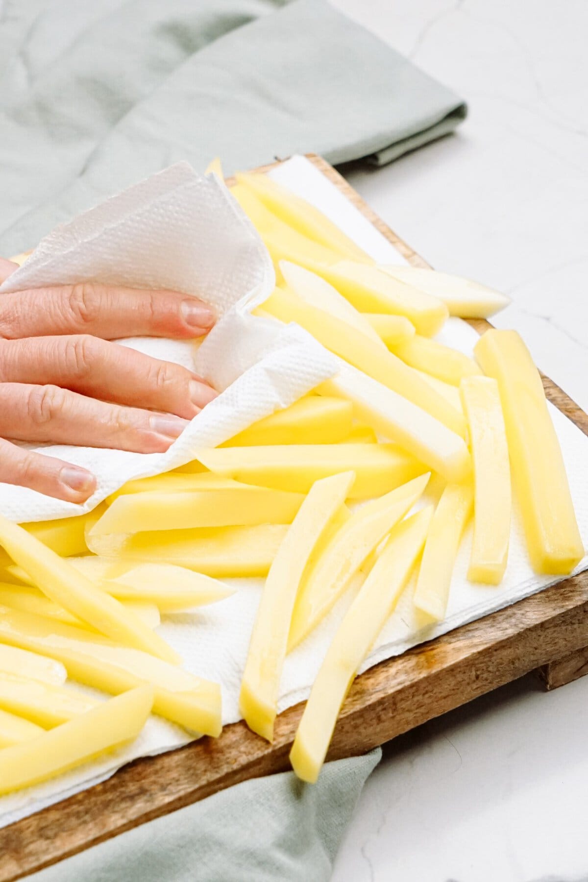a person drying off potato slices with paper towels