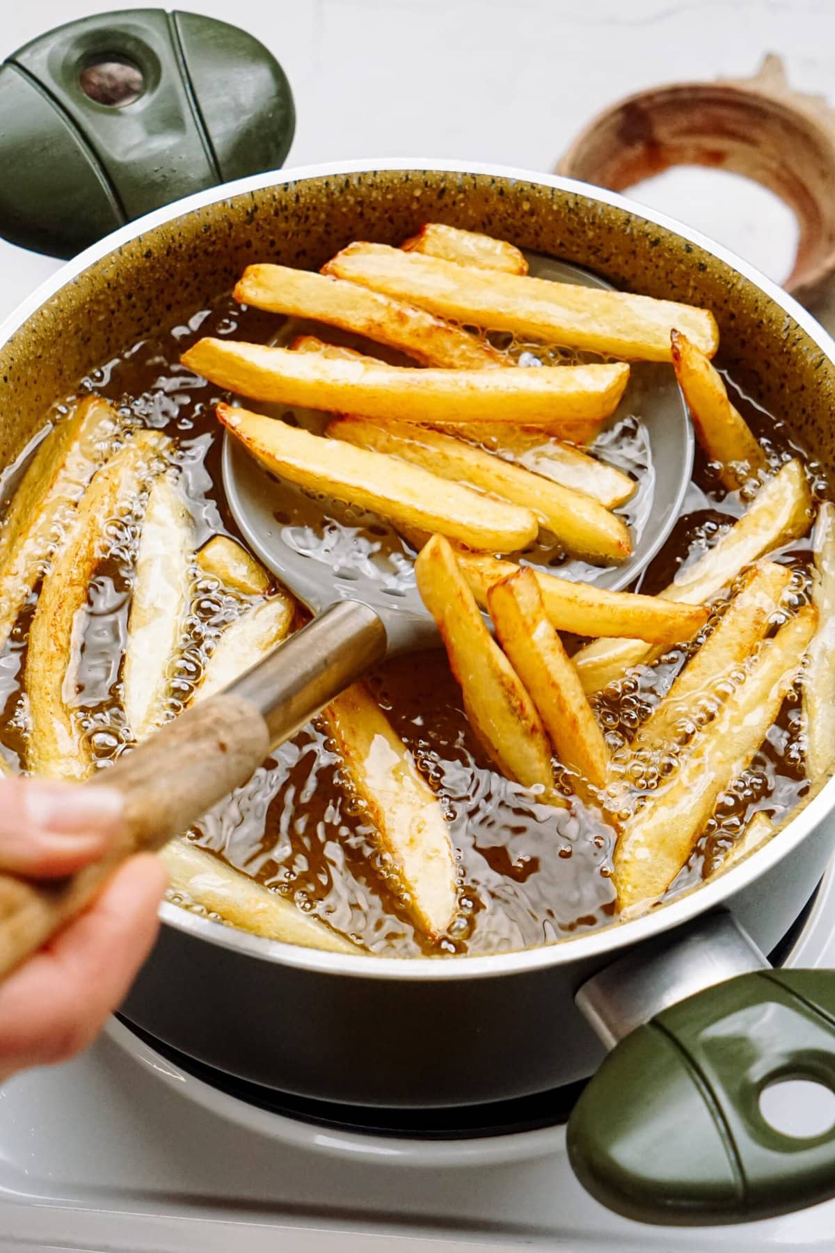 frites being removed from hot oil on a slotted spatula