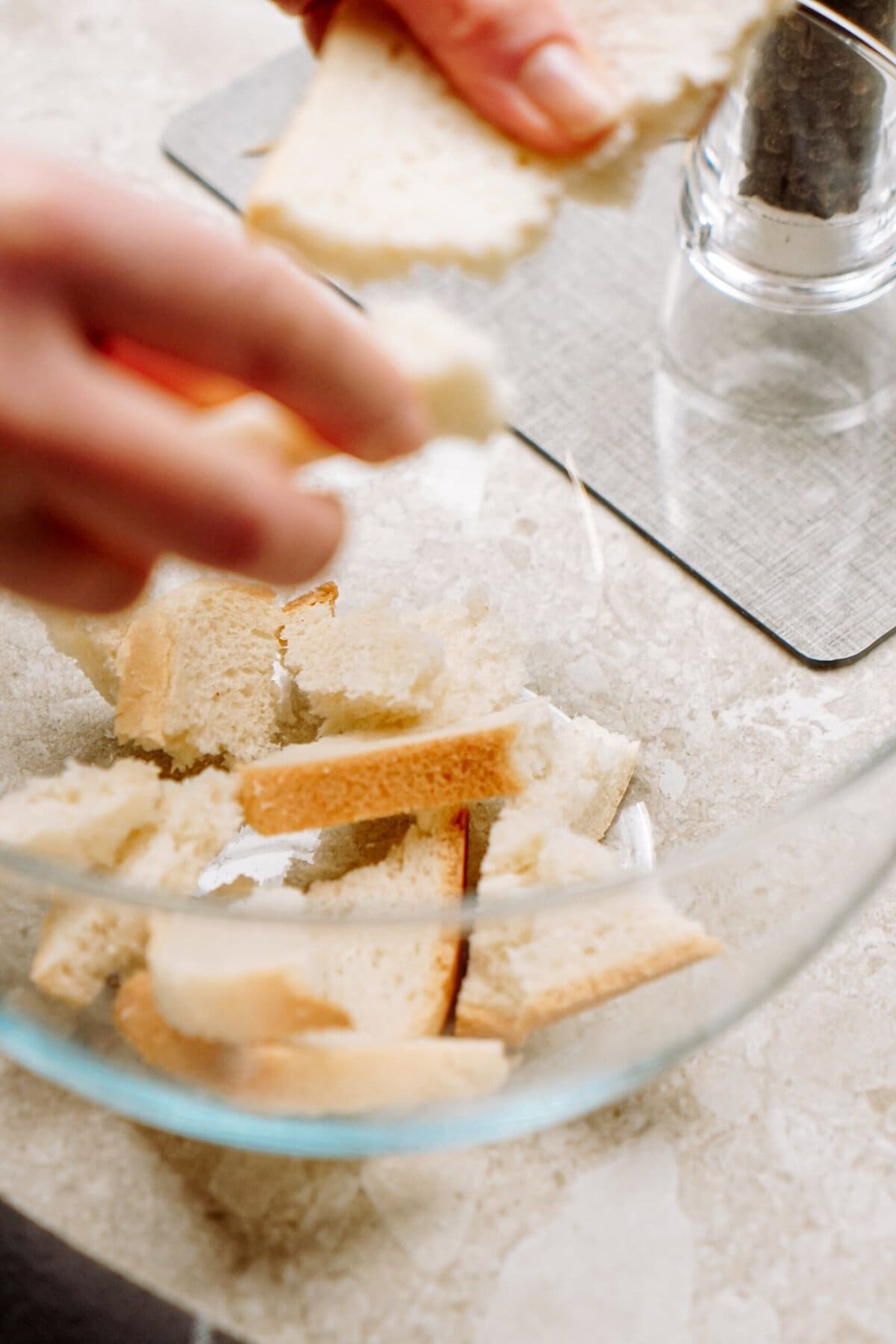 Person tearing bread into smaller pieces over a glass bowl.
