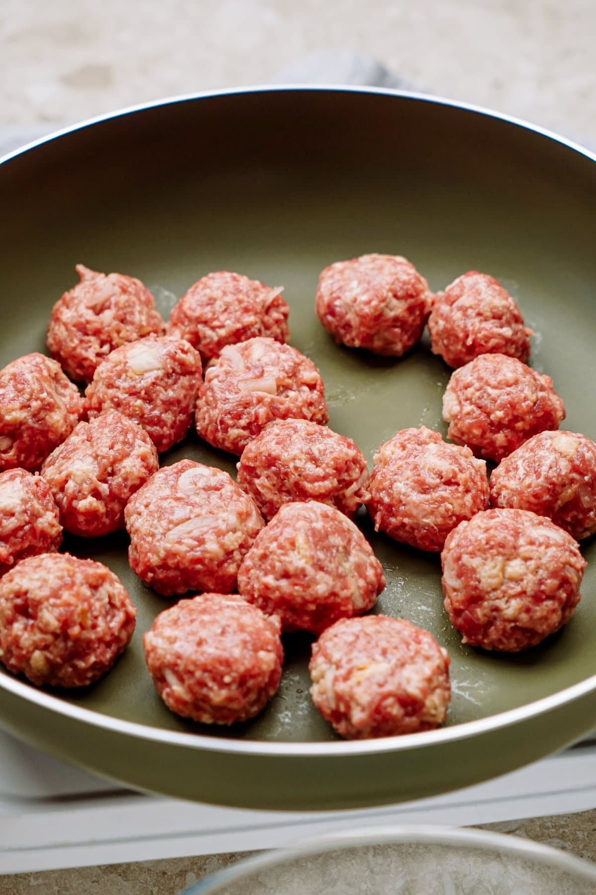 Raw meatballs arranged on a frying pan, ready to be cooked.