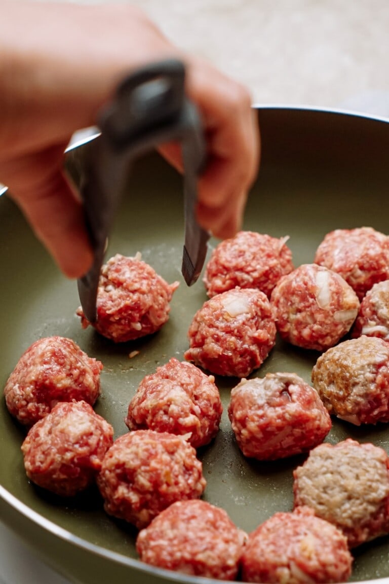 Cooking raw meatballs in a pan with tongs.