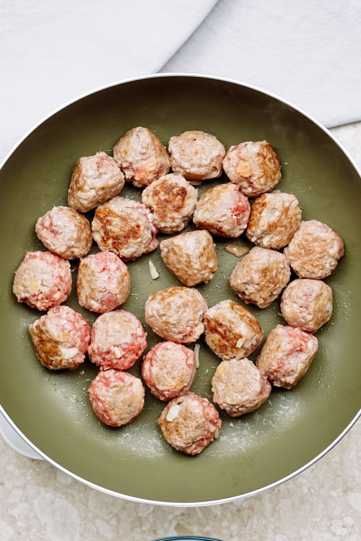 Raw meatballs partially cooked in a frying pan.