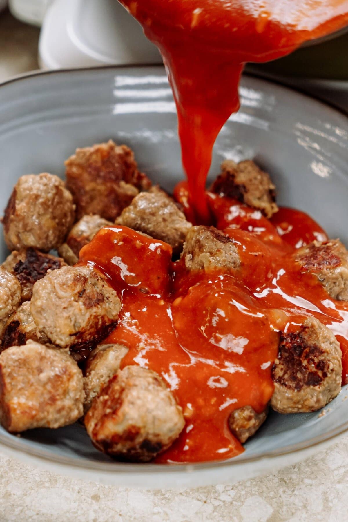 sweet and sour sauce being poured over meatballs in a bowl.
