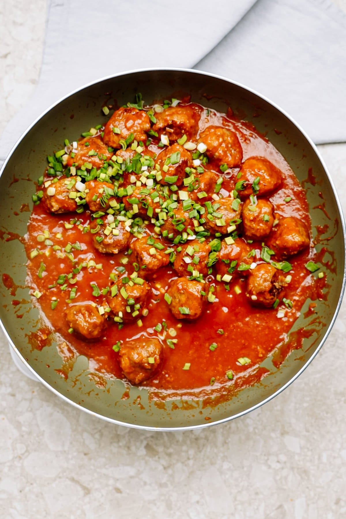 Bowl of meatballs in tomato sauce garnished with chopped herbs.