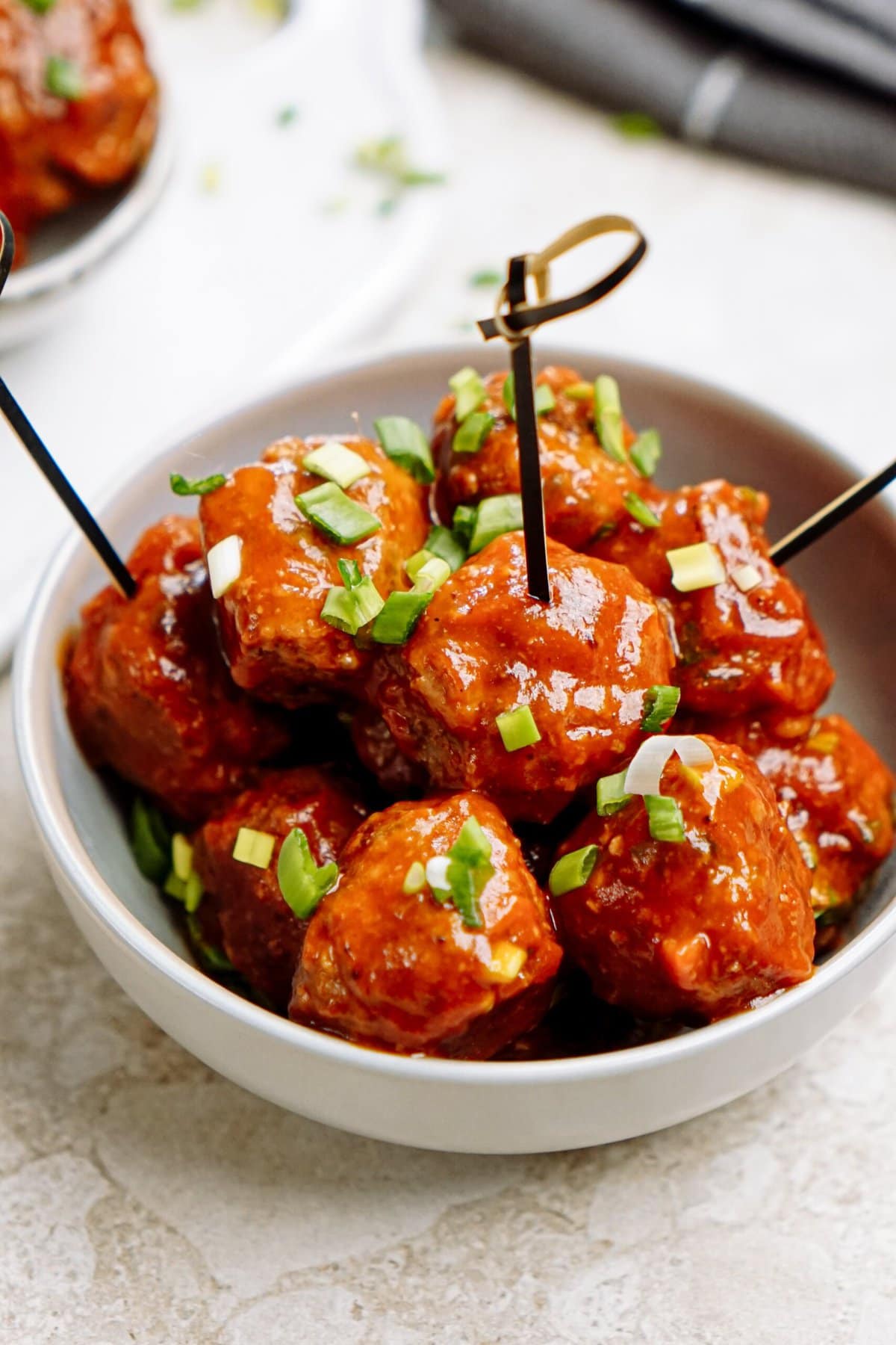 A bowl of glazed meatballs garnished with green onions.