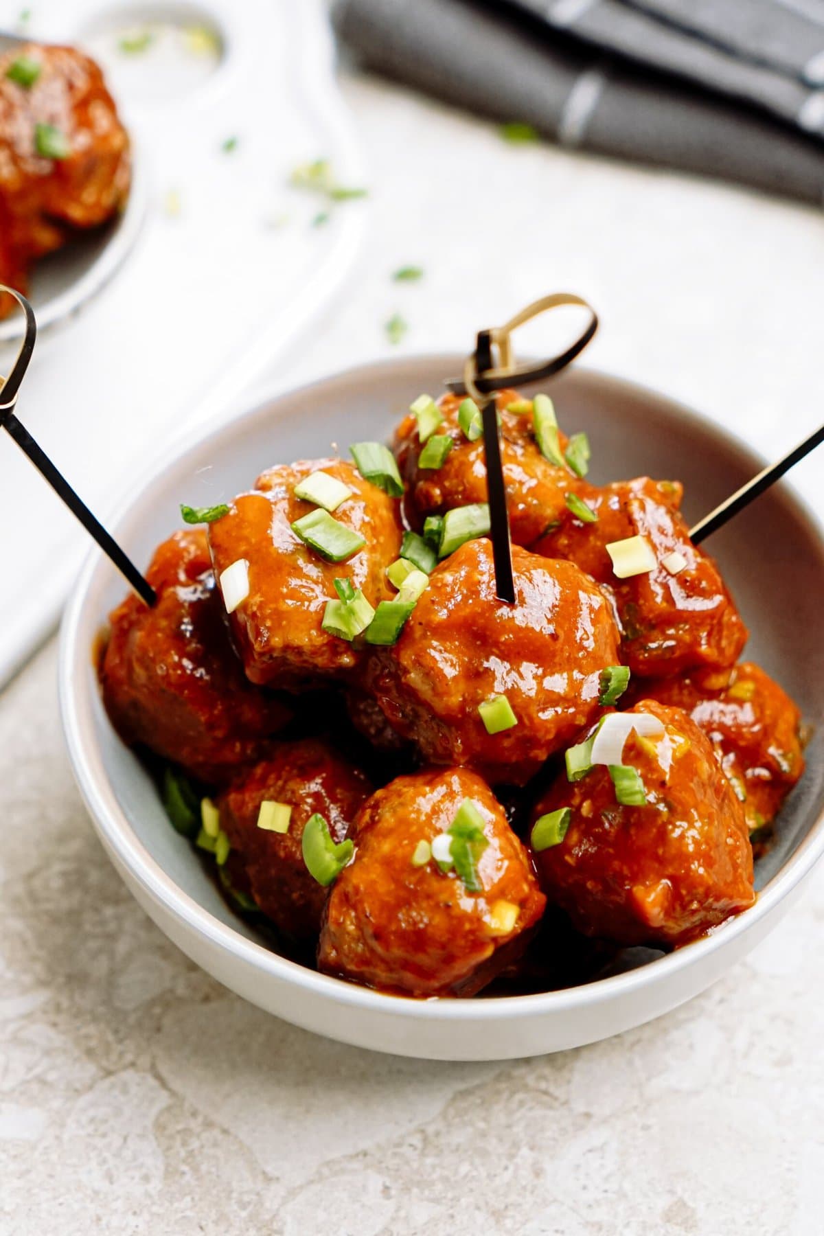 A bowl of glazed meatballs garnished with green onions, served with toothpick skewers.