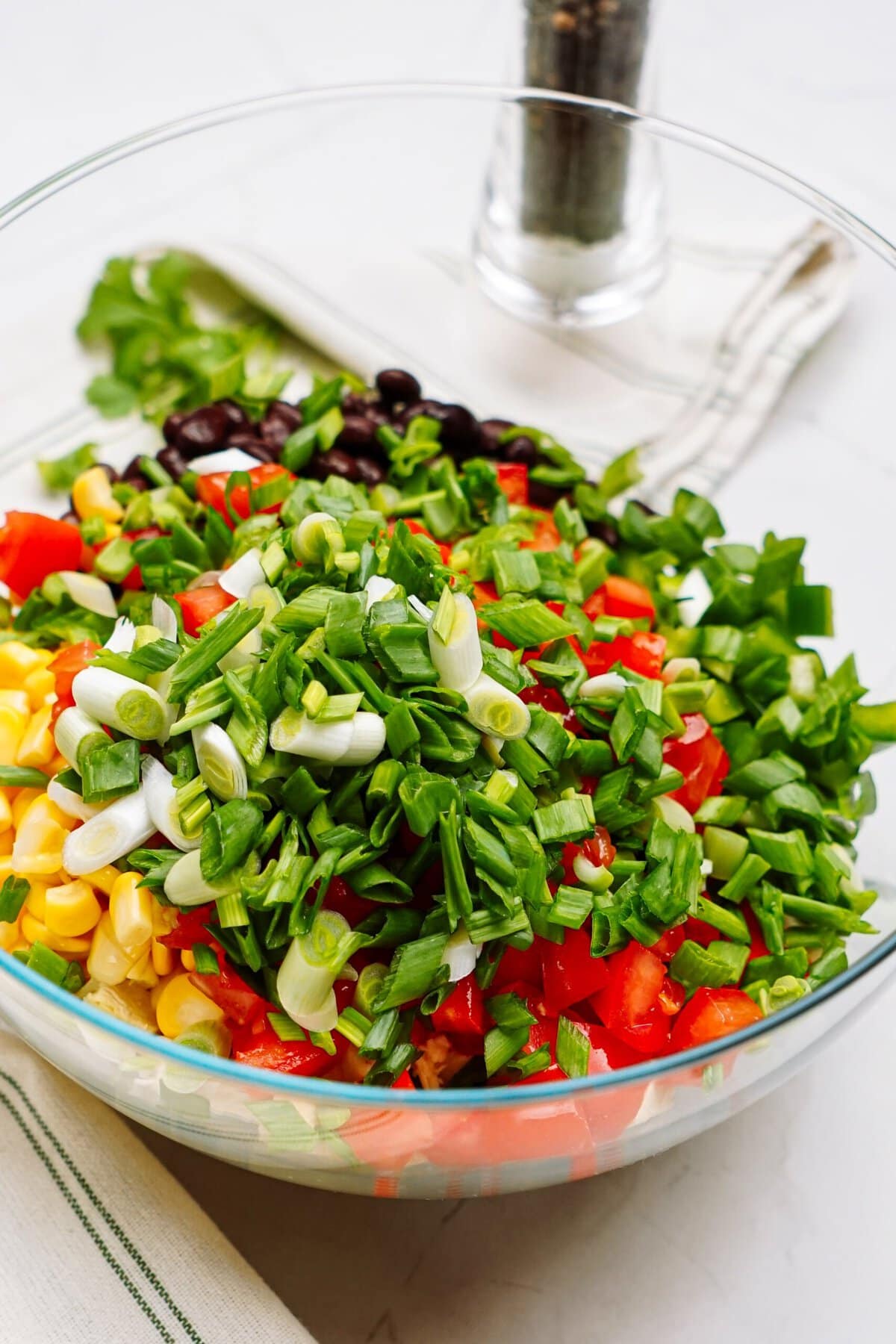 A colorful southwest layered salad with tomatoes, corn, black beans, and chopped green onions in a glass bowl.