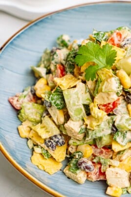 A colorful southwest chicken salad with avocado, corn, and tomatoes on a blue plate.