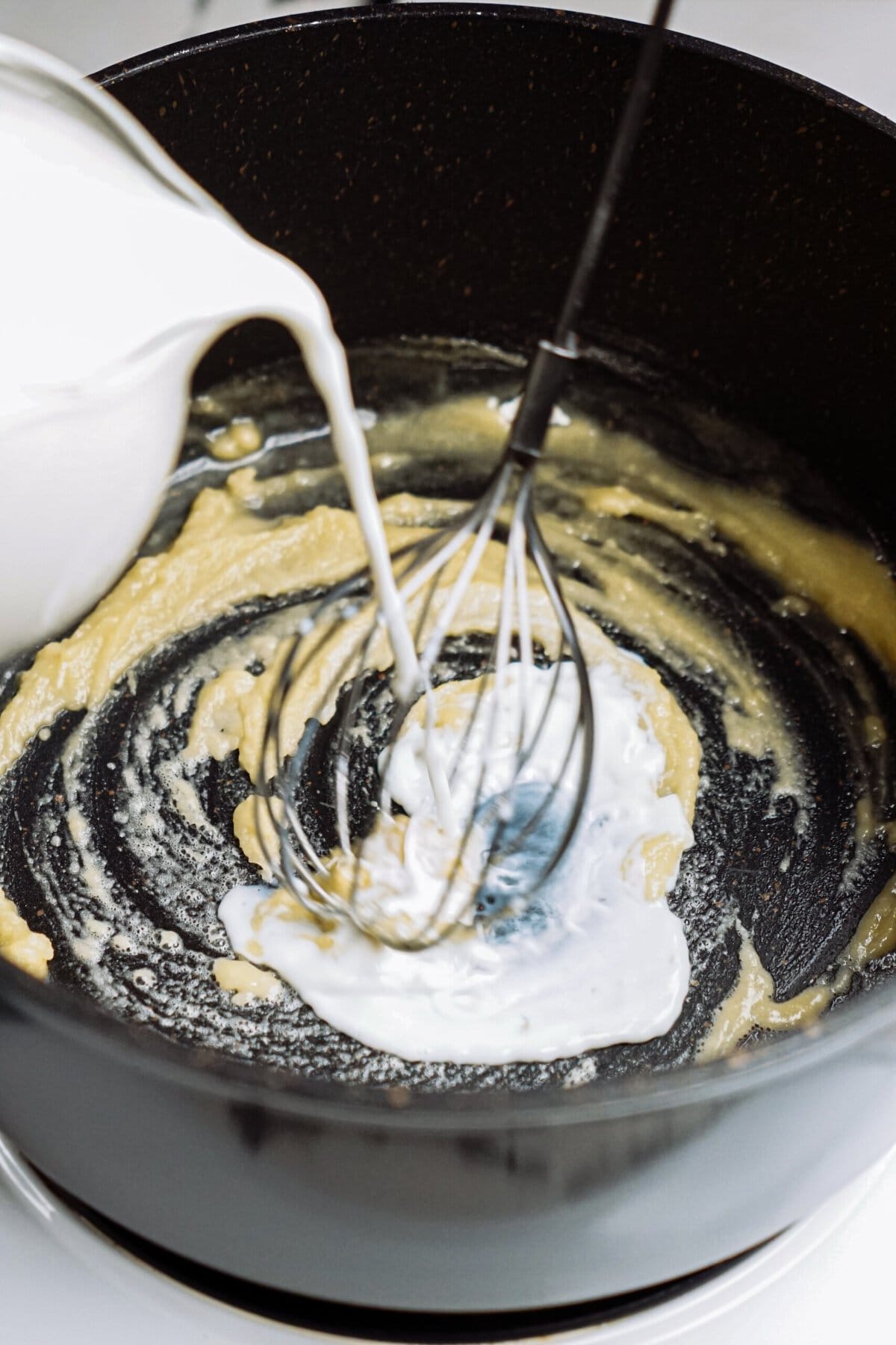 Milk being poured into a batter mixture with a whisk in a black bowl.
