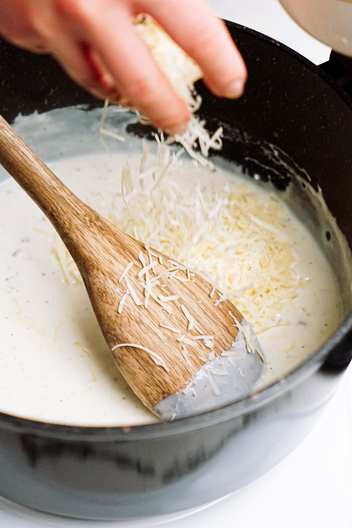 Sprinkling shredded cheese into a creamy sauce in a pan.